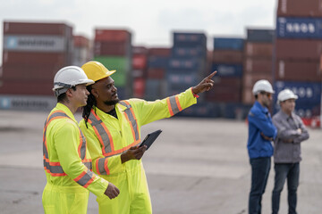 Two logistics workers in high visibility safety gear and hard hats discuss operations at a busy...
