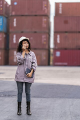 asian woman logistics workers walking to check container. operations at a busy shipping container yard. One is holding a tablet while pointing towards the cargo stacks.