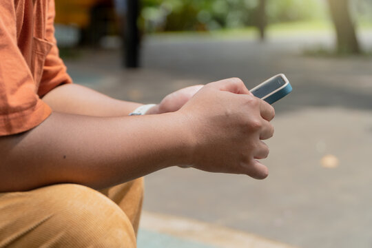 Close-up of a person using a smartphone outdoors, focusing on hands and device. Casual setting with a blurred background