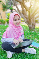 Asian Islamic children do homework with laptop on green grass, Muslim children connect internet and search information, she feeling fun and smile, education time in the garden.