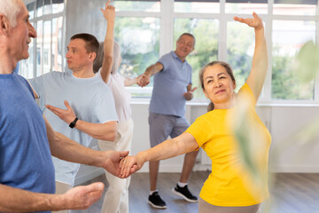 Fototapeta premium Enthusiastic emotional aged woman in sportswear attending group choreography class, learning modern vigorous dance with male partner. Seniors hobbies concept..