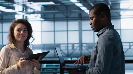 Data scientists in server room using laptop and tablet, executing security patches, verifying firewall configurations. People performing equipment vulnerability scans in data center, camera A