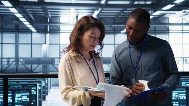 Data center engineer greeting colleague, examining system diagnostics paperwork together. Server room workers doing handshake, meeting to look over maintenance reports, camera B