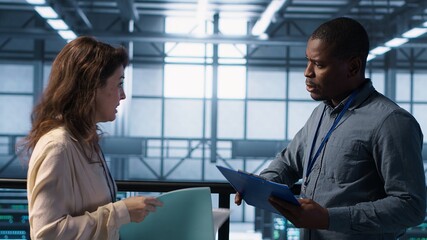 Fototapeta premium Data center engineer greeting colleague, examining system diagnostics paperwork together. Server room workers doing handshake, meeting to look over maintenance reports, camera A