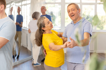 Happy smiling elderly woman enjoying impassioned merengue with male partner in latin dance class....