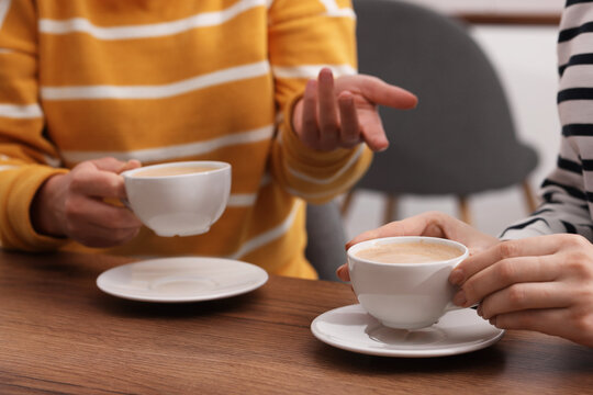 Coffee break. Women with cups of hot drinks at wooden table indoors, closeup