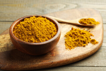 Turmeric powder in bowl and spoon on wooden table, closeup