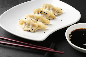 Delicious gyoza dumplings with sesame seeds served on black table, closeup
