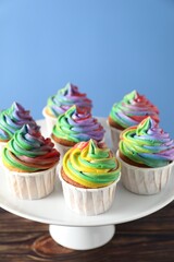 Delicious cupcakes with colorful cream on wooden table against blue background, closeup