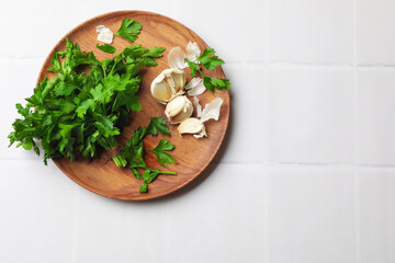 Fresh parsley and garlic on white tiled table, top view. Space for text