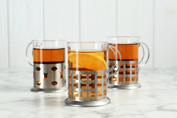 Glasses of tea in metal holders served on white marble table, closeup