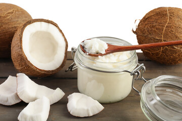 Coconuts, cooking oil and spoon on wooden table against white background