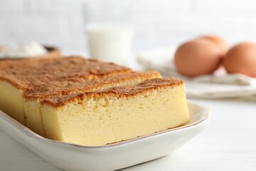 Tasty Japanese Castella sponge cake and ingredients on white table, closeup