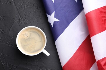 Cup of coffee and American flag on black table, top view