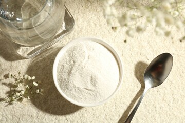Collagen powder in bowl, spoon, glass of water and gypsophila branches on light textured table,...