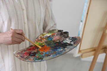 Man mixing paints on palette near easel in artist's studio, closeup