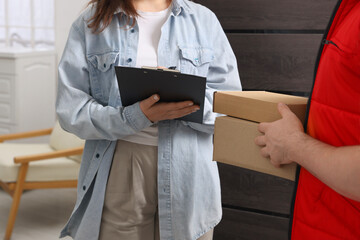 Courier with boxes and receiver signing for delivered parcels indoors, closeup