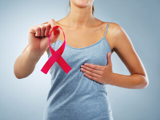 Hands, woman and ribbon in studio for breast cancer with awareness, support or touch chest by blue...