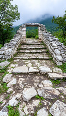 Ancient stone staircase leading to arched gateway in lush, mountainous landscape
