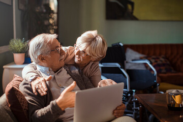 Elderly couple embracing while using laptop at home