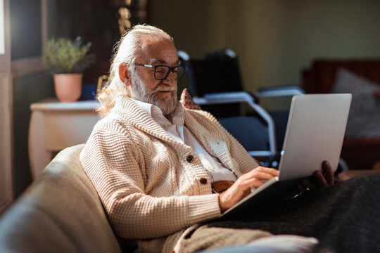 Senior man with long hair using laptop at home in cozy living room