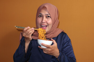 Muslim woman eating spicy instant noodles with chopsticks, enjoying delicious food