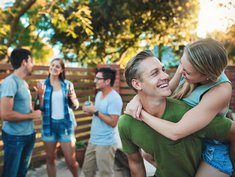 Couple, hug and patio party backyard with friends, love and outdoor at labor day and social event. Piggy back, conversation and happy people with summer fun, vacation and group with smile and care