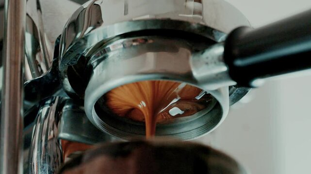 Pouring coffee stream from professional machine in cup. Barista man making double espresso, using filter holder. Flowing fresh ground coffee. 