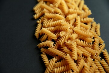 A close-up of uncooked spiral pasta scattered on a dark surface, showcasing its golden texture.