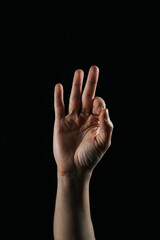 Fototapeta premium Close-up of a human hand showing three fingers up against a black background. Symbolic gesture used in communication, counting, or sign language.