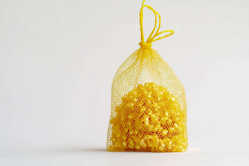 A delicate yellow mesh bag filled with shimmering golden beads, hanging by a thread against a clean white background.