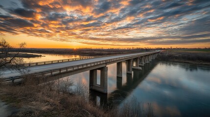 Fototapeta premium A wide highway crossing a long bridge over a river, with dramatic sky clouds above and plenty of space for highway-related text.