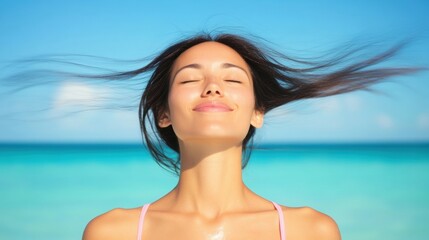A woman stands by the ocean with her eyes closed, reveling in the fresh breeze against her face, surrounded by clear blue water