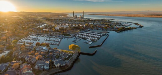 Aerial view of Pittsburg, California, USA, at sunset. The image shows the city's marina, waterfront homes, and a power plant in the distance. 