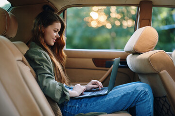 Young woman working on a laptop in a car, enjoying the moment with a relaxed expression, surrounded by soft sunlight and natural greenery background.