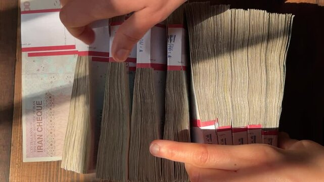 Counting Iran money bundle the biggest value banknote compare USD dollar daytime sun throw hurl forceful rial currency 100 bill versus financial fall inflation economy finance investment sell wealth