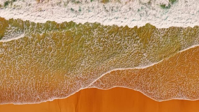 Top down drone view of Cofete Beach in Fuerteventura, Spain, showing gentle sunset waves, warm tones, clouds, and peaceful atmosphere