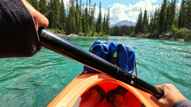 POV 4K action cam captures a kayaker paddling gently downstream on the Bow River. Surrounded by serene emerald waters and dense forest, they favour the quiet beauty of the Canadian wilderness.