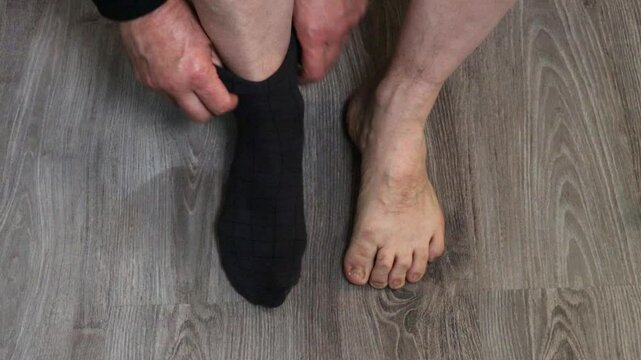 Male hands putting on dark socks on gray laminate background, top view, close-up.