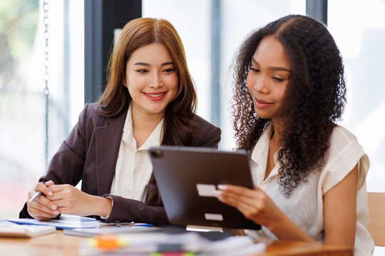 Two business women or an accountant team are analyzing data charts, graphs, and a dashboard on a laptop screen in order to prepare a statistical report and discuss financial data in an office
