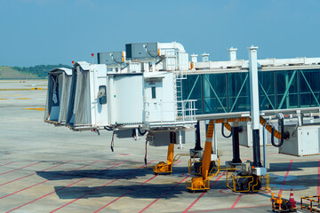 Jet bridge empty at the airport terminal and a standing plane in the distance