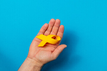 Fototapeta premium Holding a yellow ribbon as a symbol of cancer awareness and hope