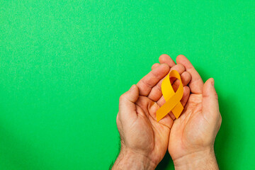 Hands holding a yellow ribbon symbolizing awareness and support for cancer