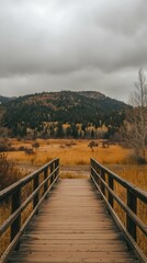 Fototapeta premium Wooden bridge leading to autumnal mountain landscape under a cloudy sky. Serene, peaceful scene.