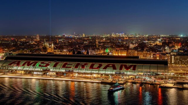 Amsterdam Centraal Station illuminated at night, with city lights reflecting on the river. A blend of historic architecture and modern urban vibrancy in the Dutch capital
