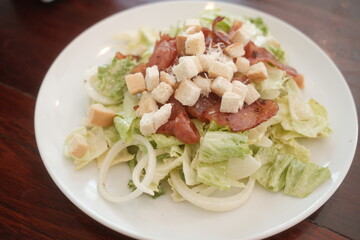 Traditional caesar salad in a white bowl with leaves and a sauce boat and parmesan. Selected focus.