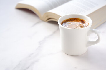 ページを開いたペーパーバック（洋書）とコーヒーの入ったコーヒーカップで、コーヒーを飲みながら読書を楽しんでいるイメージ
