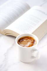 ページを開いたペーパーバック（洋書）とコーヒーの入ったコーヒーカップで、コーヒーを飲みながら読書を楽しんでいるイメージ

