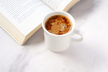 ページを開いたペーパーバック（洋書）とコーヒーの入ったコーヒーカップで、コーヒーを飲みながら読書を楽しんでいるイメージ
