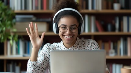 A smiling woman in headphones takes an online class, waving at her webcam. 